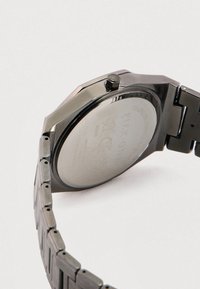 Metalluhr mit einem achteckigen schwarzen Gehäuse und einem Edelstahlarmband. Die Rückseite ist glatt mit eingravierten Markierungen und einer polierten Oberfläche.