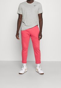Grå kortärmad Nike-t-shirt i kombination med rosa tapered sweatpants. Vita sneakers med guldaccenter och grå sulor.