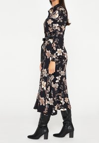 Vestido negro con estampado floral, mangas largas, pequeño cuello, cintura ceñida y falda acampanada. Flores en tonos beige y rosa. Botas negras hasta la rodilla.