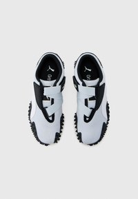 Jasnoszare buty sportowe z czarnymi akcentami, zaprojektowane jako wsuwane z teksturowaną czarną podeszwą. Dwa elastyczne paski na górze.