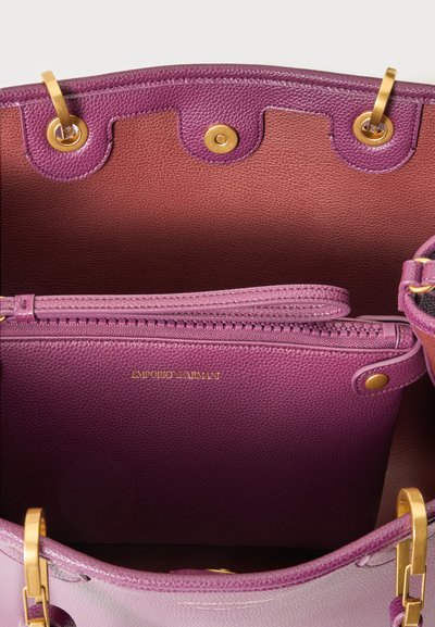 Intérieur de sac à main en cuir violet avec fermeture magnétique dorée, quincaillerie dorée et une pochette zippée assortie portant l’étiquette Emporio Armani.