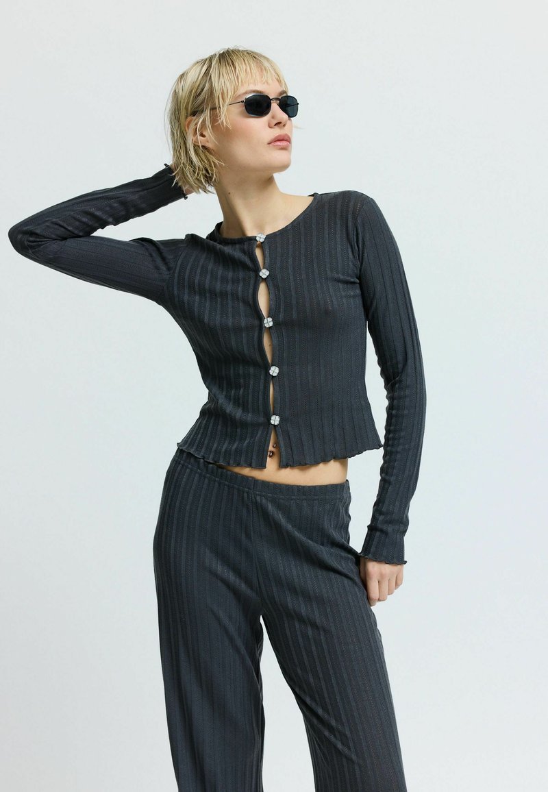 Černý žebrovaný top s dlouhým rukávem, krátkým střihem a dekorativními knoflíky, doplněný o ladící žebrované kalhoty.