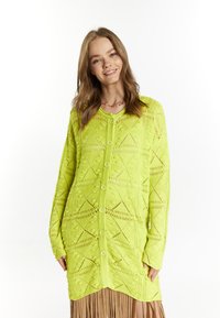 Ljus neongrön stickad cardigan med ett geometriskt mönster, långa ärmar och knappar framtill, tillsammans med en plisserad kjol.