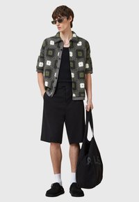 Cămașă cu mânecă scurtă în culorile verde, negru și alb, cu un model floral din croșetă, pantaloni șort negri, geantă neagră și ochelari de soare; încălțăminte casual.