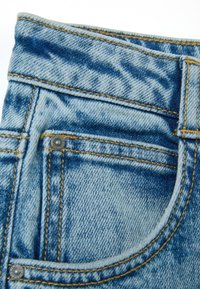 Pantalones de mezclilla azules con una vista en primer plano de la cinturilla y el bolsillo, con costuras amarillas y un detalle de botón metálico.