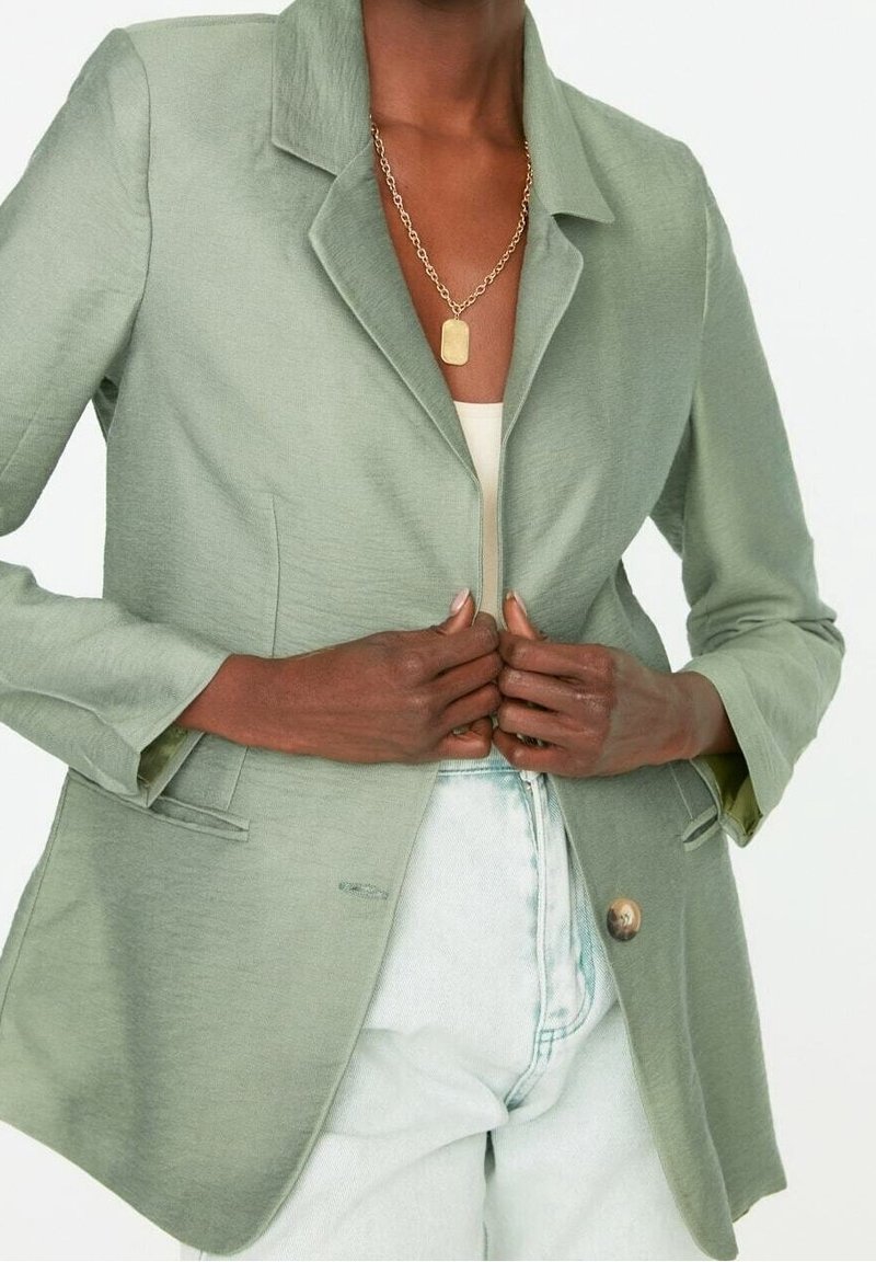 Vihreä bleiseri kevyessä kankaassa, jossa on sakara-kaulus, yksittäinen nappisulku ja kaksi etutaskua.