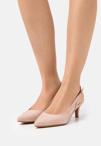 Talons slingback en daim rose avec un embout pointu et un petit talon cylindrique. Présente une sangle réglable avec un détail de boucle en or.