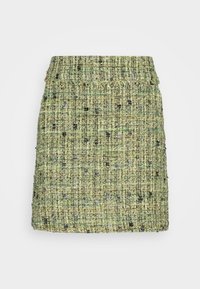 Mini-jupe en tweed vert avec un motif texturé et une finition effilochée le long de la ceinture, présentée sur un fond uni.