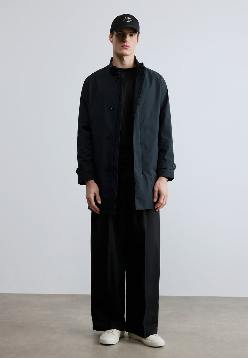 Lightweight black and dark gray jacket with button closure, worn over a black shirt. Paired with loose black pants and white sneakers.