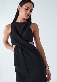 Must kleit, millel on halterkaelus, keerutatud eesmine detail ja küljedetailide lõiked. Siidine kangapind koos volditud seelikusiluetiga.