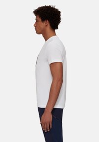 Witte t-shirt met korte mouwen en een ronde halslijn, met een gladde textuur, gedragen met marineblauwe sportbroek. Van opzij weergegeven.