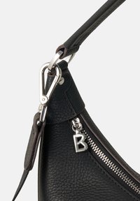 Borsa a tracolla in pelle nera con finitura texture, zip argentata e hardware metallico. Presenta un charm con la lettera "B" attaccato alla zip.
