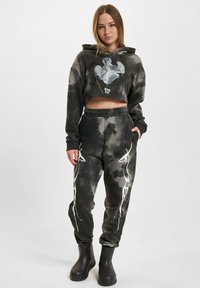 Zkrátená čierno-sivá mikina s grafickou potlačou v štýle tie-dye; zodpovedajúce joggers nohavice majú biele vzory bleskov po stranách; spárované s čiernymi čižmami.