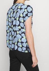 Blusa a maniche corte in tessuto blu navy con un motivo di foglie in blu chiaro e verde. Vestibilità sartoriale con spacchi sui lati dell'orlo.