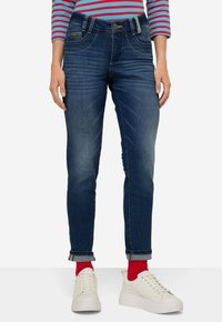 Granatowe dżinsy z średnim stanem, z podwiniętymi mankietami i kontrastowym przeszyciem. Połączone z białymi sneakersami i czerwonymi skarpetkami.