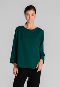 Tiffany zöld blúz kerek nyakkal és háromnegyedes ujjal. Simaságát igényes anyag adja, laza fazonú, finom oldalsó slitjeivel.