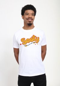 Hvid bomulds t-shirt med fed gul "Sooty" tekst, blå slogan og røde detaljer. Simpelt crew neck design med korte ærmer.