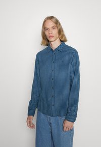 Camisa de cuadros azul y negra con botones, hecha de una tela suave, de mangas largas y con cuello. Presenta botones negros y un corte relajado.
