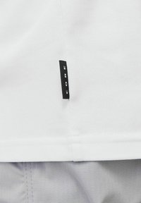 Hvidt tekstureret stof med en sort label, der står "CORE" ved sømmen. Den nederste kant er pænt afsluttet med en lige kant.