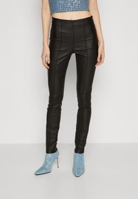 Fekete műbőr nadrág, slim fit fazonnal és elülső varrásokkal, világoskék, texturált bokacsizmával párosítva, amely ezüst kiegészítőkkel rendelkezik.