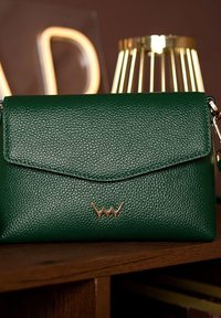 Zelená kožená kabelka s texturou, s klopovým uzávěrem, zlatými kovovými detaily a odnímatelným popruhem. Kompaktní obdélníkový tvar.