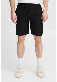 Shorts en lin noir avec une taille élastique et un cordon de serrage. Le modèle porte des chaussettes blanches aux chevilles et des baskets claires. Conception simple et droite.