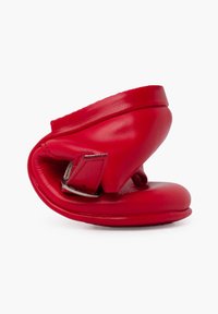 Zapato de cuero rojo con una forma única y curvada. Cuenta con una correa de hebilla lateral y una textura suave, mostrando un diseño moderno.