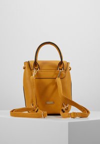 Żółty plecak z imitacji skóry o przemyślanej konstrukcji, z dwoma górnymi uchwytami i regulowanym paskiem na ramię. Wyposażony w złote akcenty metalowe.