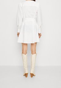 Vit bomulls klänning med en figurnära överdel, utsvängd kjol och midjeband. Långa ärmar med knappmanchetter. Bärs med knähöga krämfärgade cowboyboots.