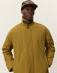 Olivno zelena, lahka jakna z visokim ovratnikom, z gumbi in stranskimi žepi. Nosijo jo z rjavim pokrivalom, ki ima vezeno besedilo.