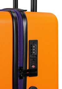 Twarda walizka w jaskrawym pomarańczowym kolorze, z fioletowym zamkiem błyskawicznym, czarnymi akcentami i zamkiem szyfrowym z boku. Teksturowana powierzchnia.