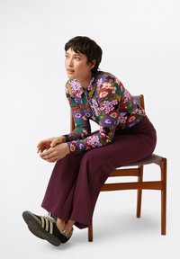 Camicetta a maniche lunghe con stampa floreale colorata realizzata in un tessuto leggero. Abbinata a pantaloni larghi a vita alta di un profondo bordeaux scuro e scarpe da ginnastica nere.