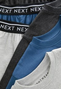 Quatre pièces de vêtements : deux grises, une gris foncé et une bleue. Chacune a un col ou une taille côtelée. L'étiquette indique "NEXT".