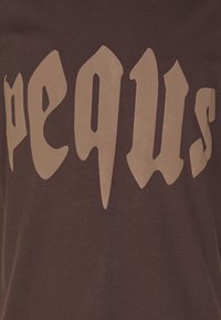 Brown fabric with large, stylized beige letters spelling "pequ s" across the surface in an angular, gothic font.