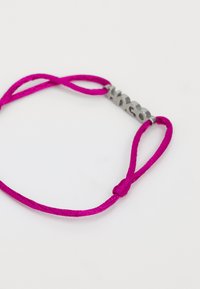 Bracelet tressé rose avec un centre métallique argenté présentant des lettres en relief, sécurisé par des nœuds réglables à chaque extrémité.