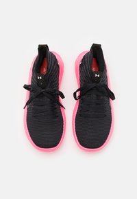 Een paar zwarte hardloopschoenen met gebreide bovenkant, zwarte veters en felroze zolen, van bovenaf gezien op een witte achtergrond.
