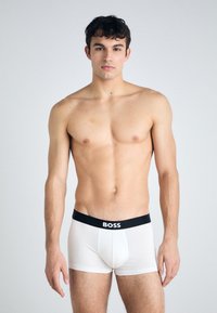 Weiße Boxer-Briefs mit einem schwarzen elastischen Bund, auf dem "BOSS" in weißer Schrift steht. Das Material wirkt glatt und eng anliegend.