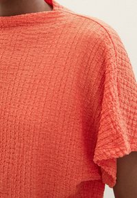 Top corto a maniche corte in corallo, con un motivo ondulato e una vestibilità ampia e rilassata, che enfatizza il tessuto morbido e il design casual.