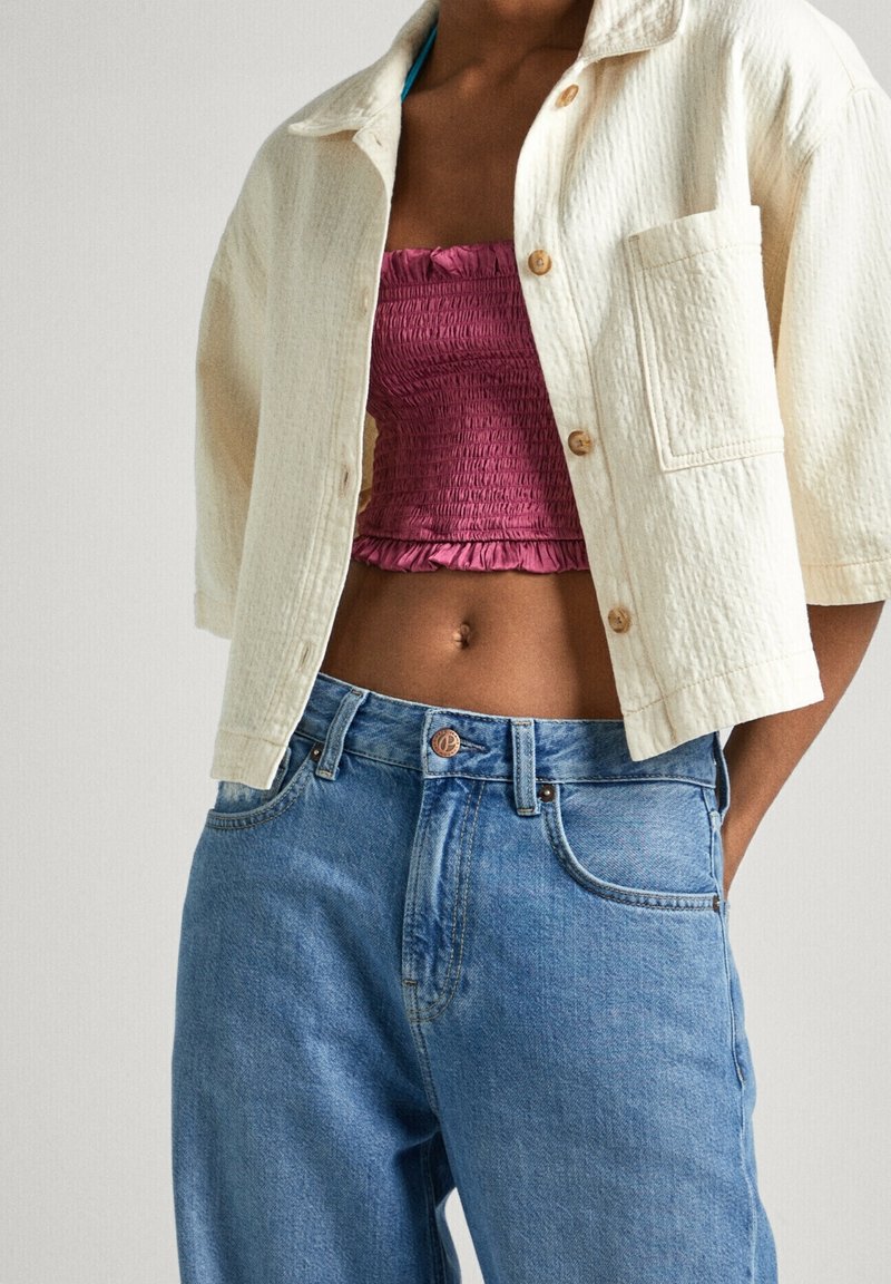 Chemise à manches courtes à texture crème avec boutons en bois, associée à un haut court froncé bordeaux et un jean taille haute bleu clair.