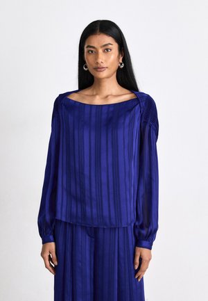 Royal blå bluse med vertikale striper og puffede ermer. Har en bred, firkantet utringning og myk, flytende stoff.