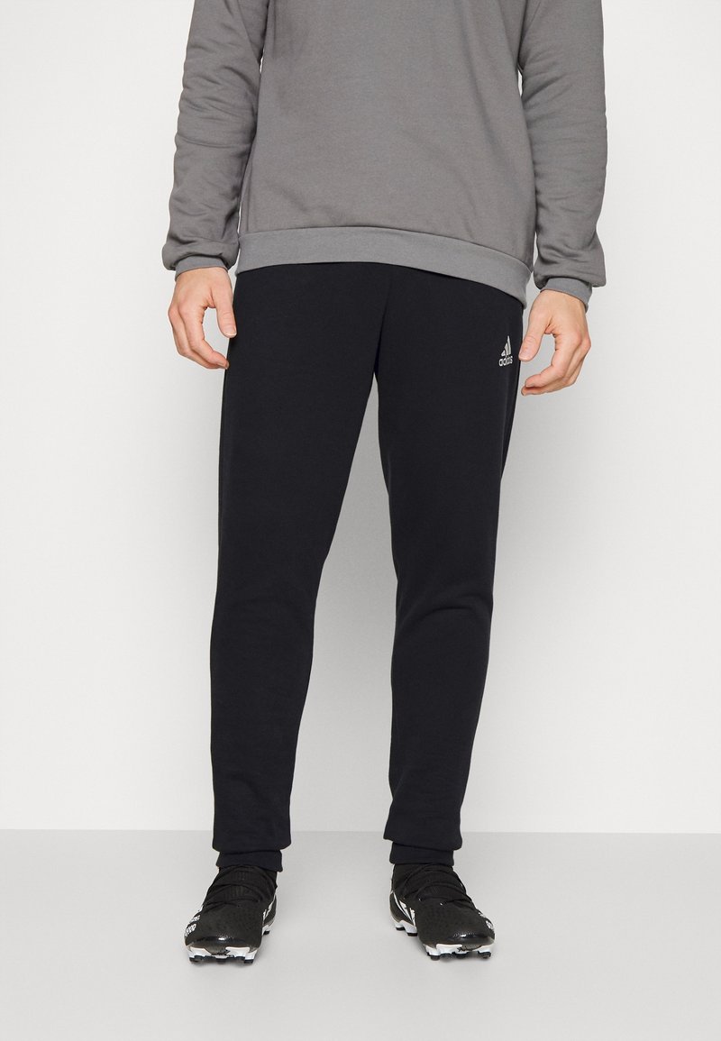 Pantalons de sport noirs en tissu doux, présentant une coupe ajustée et une taille élastique. Associés à des chaussures de sport noires.