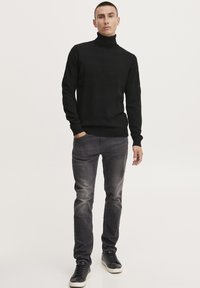 Schwarzer Rollkragenpullover mit strukturiertem Paneeldesign, kombiniert mit grauen Slim-Fit-Jeans und schwarzen Sneakers. Minimalistischer Stil, neutrale Farben.