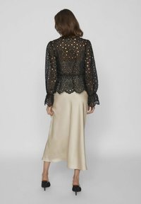 Blusa nera in pizzo con ritagli floreali e maniche a sbuffo, abbinata a una gonna midi in satin beige, che presenta una silhouette fluida.
