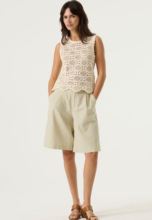 Débardeur en crochet crème à motif floral, associé à un short ample vert clair. Le modèle porte des sandales marron.