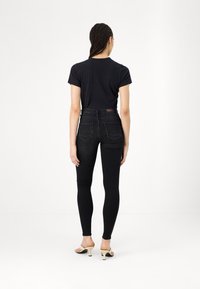 Høj talje sorte jeans med slim fit og diskrete baglommer, parret med en sort t-shirt med korte ærmer og beige hælede sandaler.