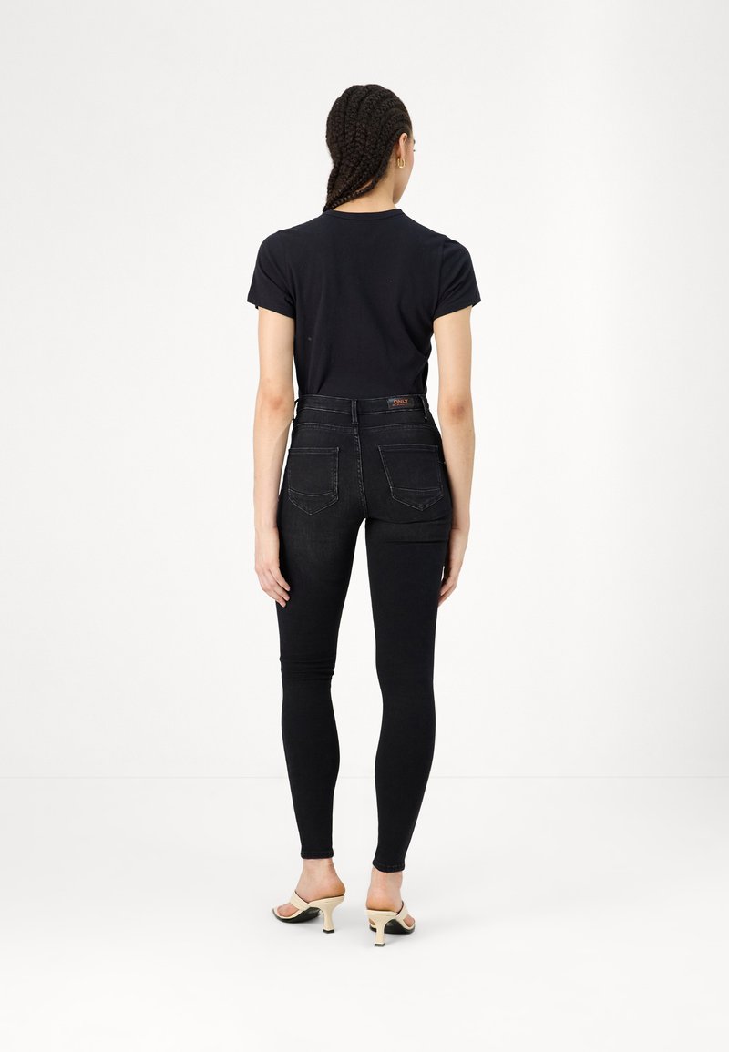 Jean noir taille haute avec coupe slim et poches arrière discrètes, associé à une chemise noire à manches courtes et des sandales à talons beiges.