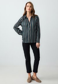 Koszula z długim rękawem, zapinana na guziki, w pionowe zielone, różowe i kremowe paski; miękka tkanina; zestawiona z czarnymi spodniami i beżowymi butami na slip-on.