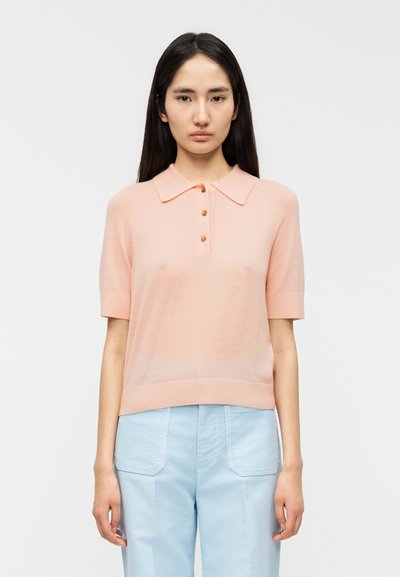 Polo rose pâle à manches courtes avec col, doté de trois boutons et d'un ourlet et de poignets côtelés. Texture lisse et maille légère.