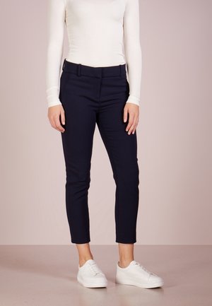 Pantalons ajustés bleu marine dotés d'une coupe slim, de poches latérales et d'une texture lisse, associés à des baskets blanches.