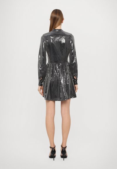 Abito nero con paillettes, maniche lunghe, vita stretta e gonna plissettata. Presenta ritagli ai polsi e arriva sopra la coscia.